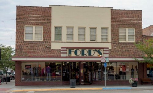 Front view of a brick building with "FORD'S" sign, showcasing a clothing store with large windows and a sidewalk.
