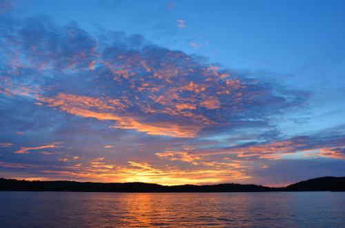 A vibrant sunset over a calm lake, with colorful clouds reflecting in the water and silhouettes of distant hills.