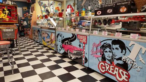 Retro diner interior with checkered floor, colorful ice cream counters, and vintage decor featuring "Grease" themes.