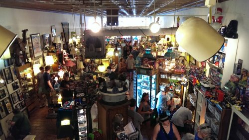 A bustling vintage shop filled with people browsing various collectibles and memorabilia under warm lighting.