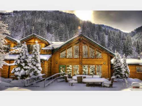 A cozy log cabin surrounded by snow-covered trees and mountains, with large windows reflecting the winter landscape.