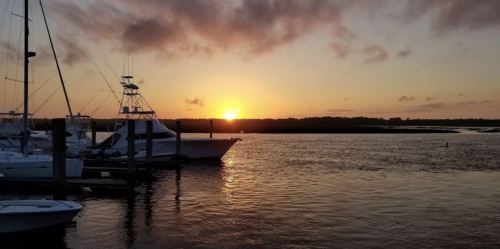 Sunset over a calm marina with boats docked, reflecting warm colors on the water.