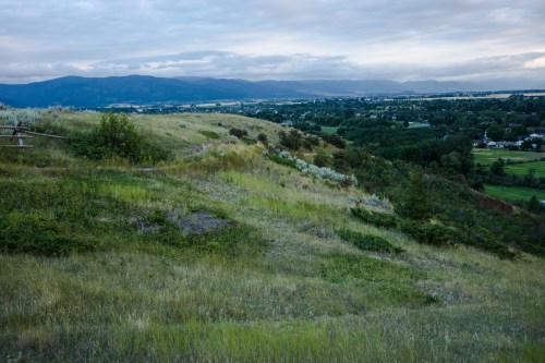 A scenic view of rolling hills and valleys under a cloudy sky, with distant mountains and a lush landscape.