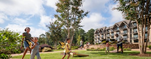 A family enjoys a sunny day outdoors, playing with butterfly props in a landscaped area near a hotel.
