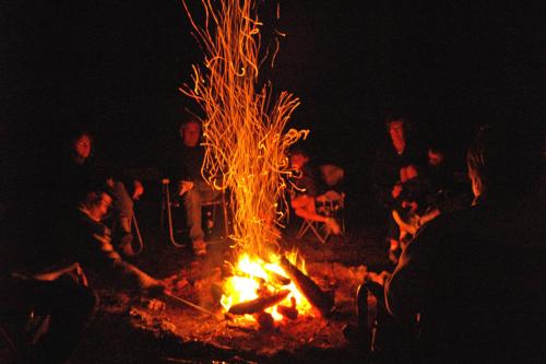 A group of people gathered around a campfire at night, with sparks rising into the dark sky.