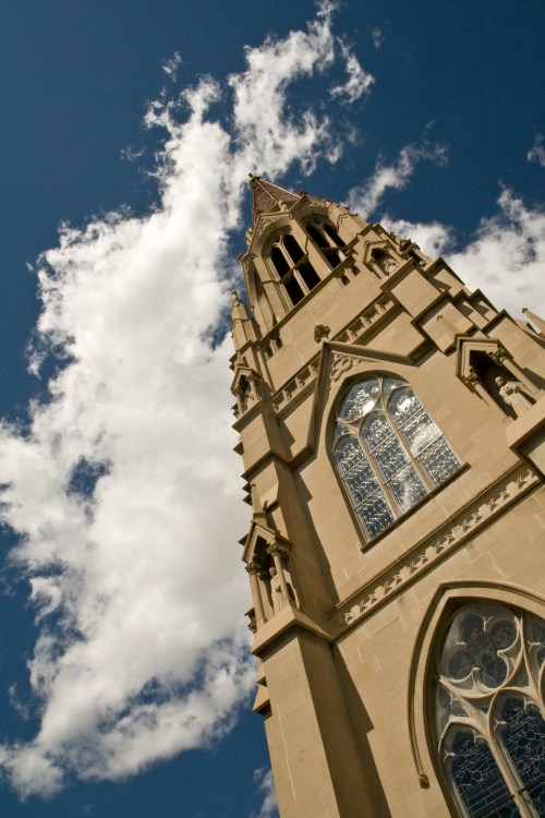 A tall church tower reaches towards a blue sky with fluffy white clouds, showcasing intricate architectural details.