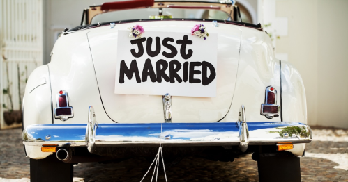 A vintage convertible car with a "Just Married" sign and flowers attached to the back.