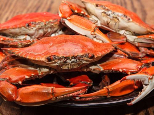 A close-up of cooked red crabs piled on a plate, showcasing their vibrant color and detailed texture.