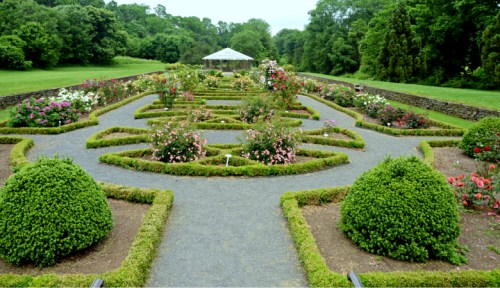 A beautifully landscaped garden with a maze of flower beds, trimmed hedges, and a gazebo in the background.