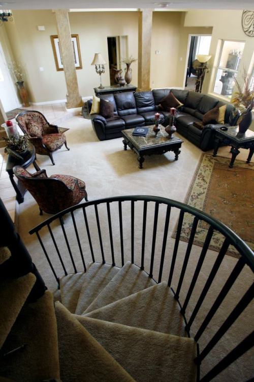 A spacious living room with dark furniture, a staircase, and decorative accents, viewed from above.