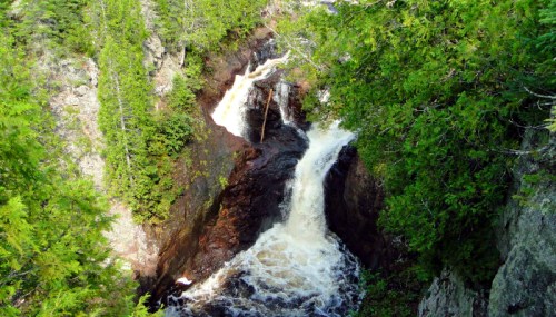 A cascading waterfall flows through rocky terrain, surrounded by lush green trees and foliage.