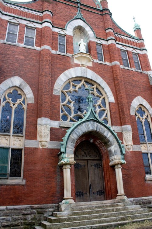 Historic brick church facade with ornate windows and a decorative entrance, featuring a statue above the doorway.