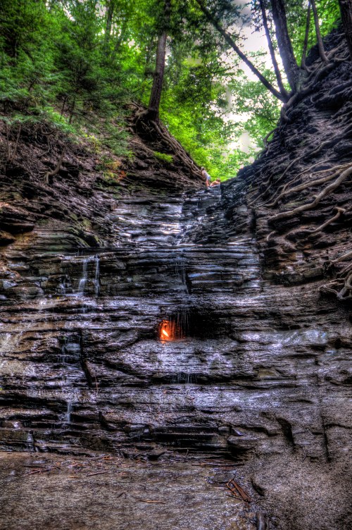 A cascading waterfall flows down a rocky cliff, surrounded by lush green trees and natural foliage.