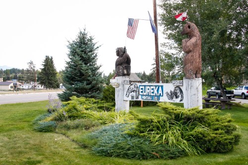 Sign welcoming visitors to Eureka, featuring bear sculptures and flags, surrounded by greenery.