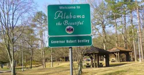 Welcome sign for Alabama, featuring "Alabama the Beautiful" and "Governor Robert Bentley," surrounded by trees and park area.