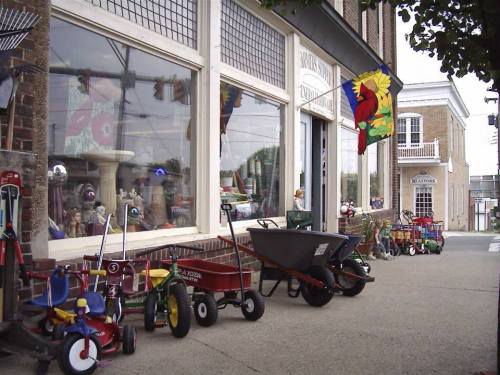 A sidewalk display of colorful children's toys and wheelbarrows outside a store with large windows.