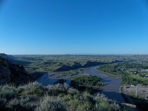 A panoramic view of a winding river surrounded by green hills under a clear blue sky.