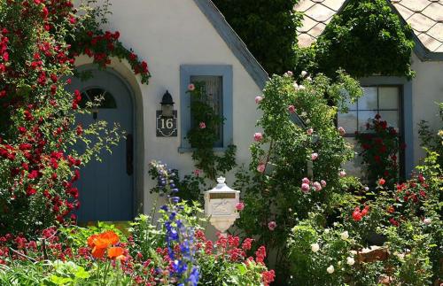 A charming cottage surrounded by vibrant flowers and climbing roses, with a blue door and a white mailbox.