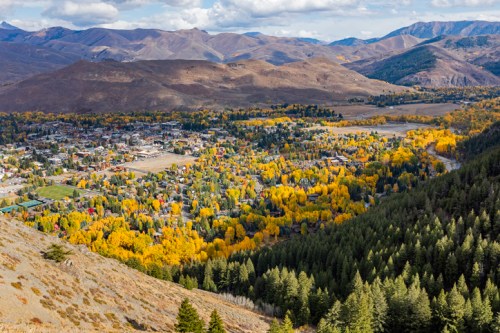 Aerial view of a valley with colorful autumn trees, mountains in the background, and a small town nestled below.