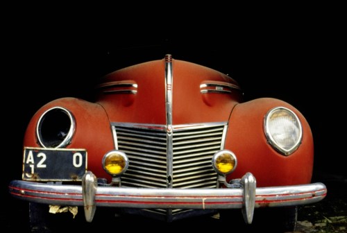 A vintage red car with chrome details, partially illuminated against a dark background.
