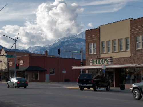 A small town street with shops, a black truck, and mountains in the background under a cloudy sky.