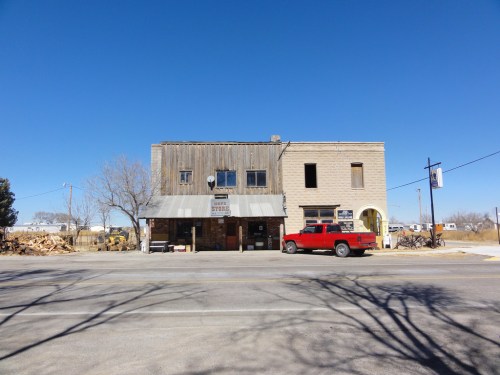 A rustic, two-story building with a wooden facade and a red truck parked in front, set against a clear blue sky.