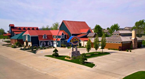 A colorful building complex with a red roof, landscaped grounds, and a prominent sign in a suburban setting.