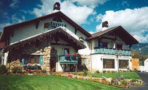 A charming two-story building with a stone facade, balconies, and colorful flower beds under a blue sky with clouds.