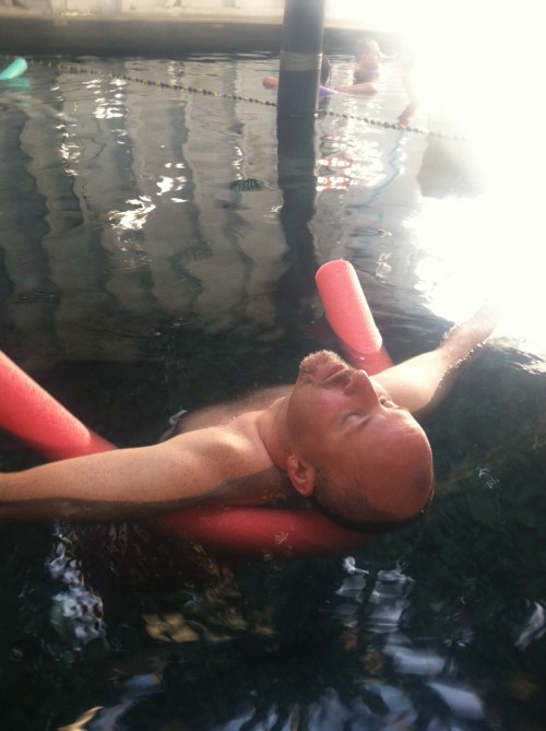 A person floats in a pool, using foam noodles for support, with a relaxed expression on their face.