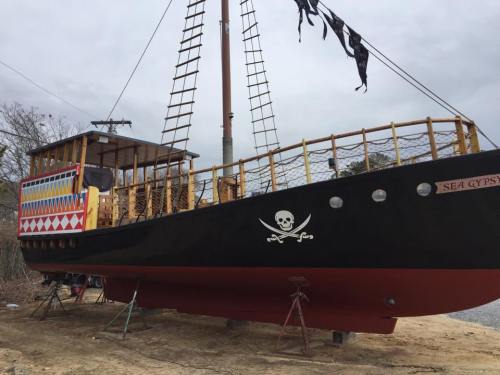 A colorful pirate ship named "Sea Gypsy" on land, with a black hull and decorative patterns, under a cloudy sky.