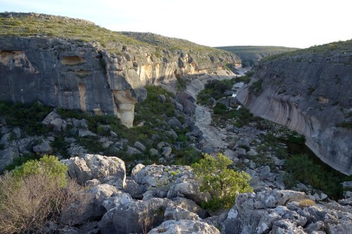 A scenic view of a rocky canyon with steep cliffs and a winding river at the bottom, surrounded by greenery.