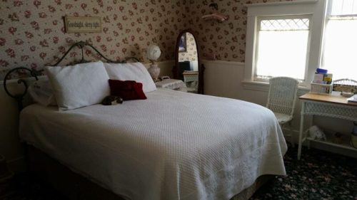 Cozy bedroom with a floral wallpaper, a large bed, a mirror, and a small chair by the window.