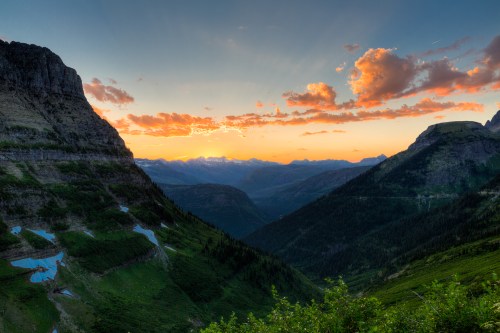 A breathtaking sunset over a mountainous landscape, with vibrant clouds and valleys bathed in warm light.