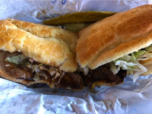 A close-up of two sandwiches with meat, lettuce, and pickles on a paper wrapper.