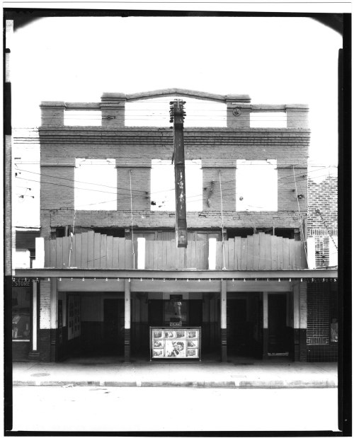 Black and white image of a building facade with missing windows and a large sign, featuring a storefront below.