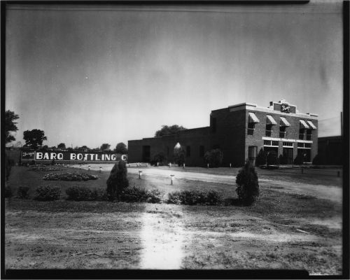 Black and white photo of Barq Bottling Company building with a sign and landscaped area in front.