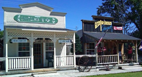 Two vintage-style storefronts: a barbershop on the left and a general store on the right, set against a clear blue sky.