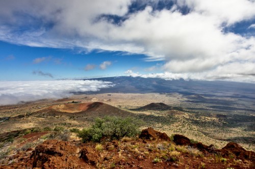 A panoramic view of a volcanic landscape with rolling hills, clouds, and a blue sky in the background.