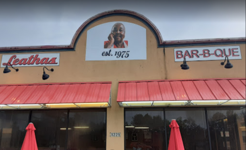 Exterior of Leatha's Bar-B-Que, featuring a sign with "est. 1975" and a smiling portrait above the entrance.