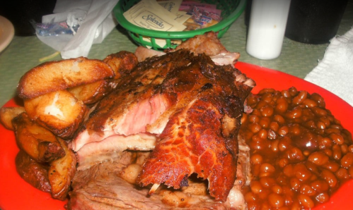 A plate of barbecue meat, baked beans, and potato wedges, served in a red dish.