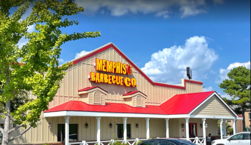 Exterior of Memphis Barbecue Co. featuring a red roof and bright signage under a blue sky with clouds.