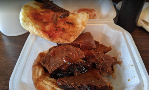 A styrofoam container with tender beef in sauce and a piece of flatbread on top.