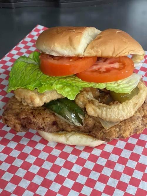 A crispy chicken sandwich with lettuce, tomato, and pickles on a toasted bun, served on a red and white checkered paper.