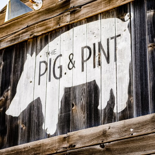 Sign featuring a pig silhouette and the text "The Pig & Pint" on a rustic wooden background.