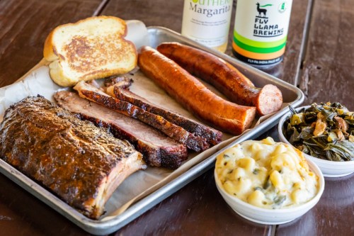 A platter of barbecue featuring brisket, sausage, macaroni and cheese, collard greens, and toasted bread.