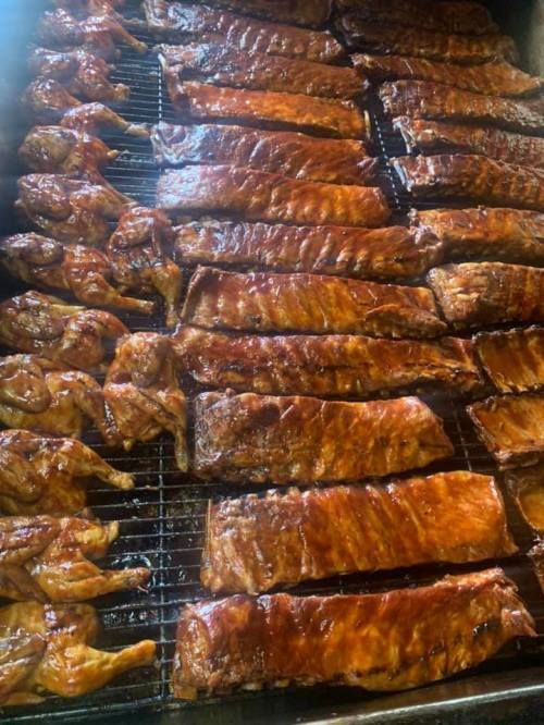 A close-up of a grill filled with smoked chicken and racks of barbecue ribs, all glistening with sauce.