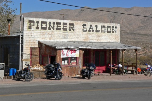 A rustic building labeled "Pioneer Saloon" with motorcycles parked outside, set against a mountainous desert backdrop.
