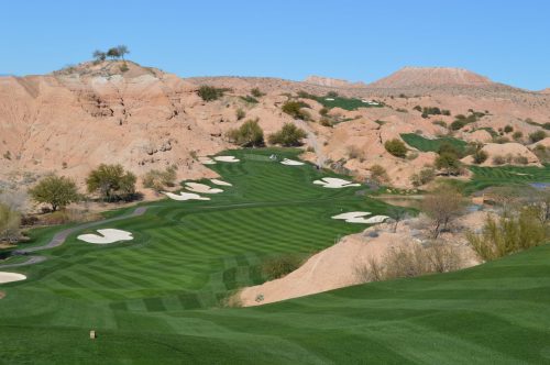 A scenic golf course with lush green fairways and sandy hills under a clear blue sky.