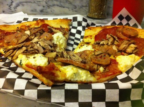 Two slices of pizza on a checkered paper, topped with meats, cheese, and sauce.
