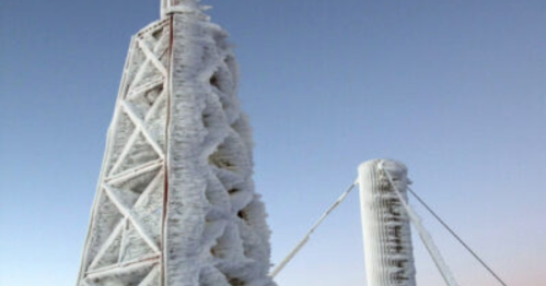 Two tall structures covered in ice against a clear blue sky, showcasing a winter landscape.